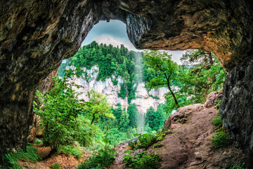 Beautiful scenic summer landscape of a rock in Kurdzhips gorge viewed from inside a weird rocky grotto with waterfall in Caucasus mountains, Russia