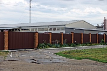 Fototapeta na wymiar коричневый забор и железные ворота перед промышленным складом у дороги