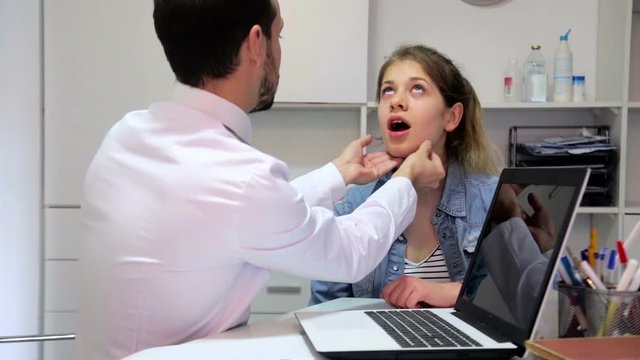 Teenage female visitor consulting male doctor about cold and sore throat
