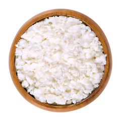 Coconut puree in wooden bowl. Grated flesh and meat of coconut kernels. White, edible and raw food paste and cream. Isolated macro food photo close up from above on white background.