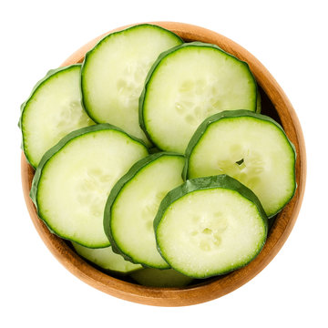 Cucumber slices in wooden bowl. Cucumis sativus. Sliced seedless vegetable, fresh and unripe with green skin. Isolated macro food photo close up from above on white background.