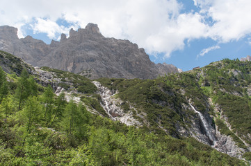 Naklejka na ściany i meble Waterfall at the foot of the dolomitic peaks and mountain hut, Dolomites, Italy