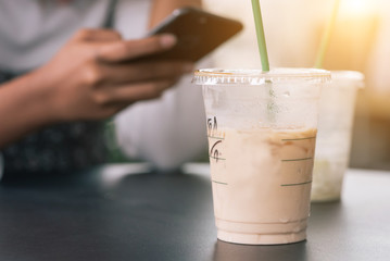 A woman using the phone until the iced coffee on the table melts in selective focus and focus at the coffee.