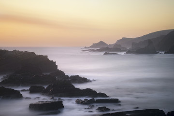 Beautiful long exposure landscape image of sea over rocks during vibrant sunset