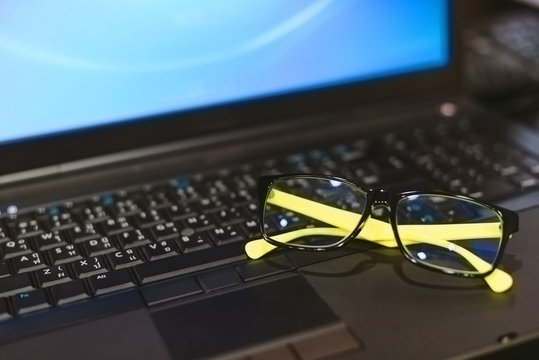 Green glasses place on the black laptop in selective focus.