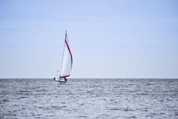 Naklejka premium Calm relaxing image of sailing boat in soft blue sky with red sail detail