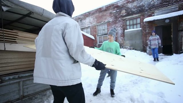Young people unload a car with plywood in winter
