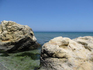 Fototapeta na wymiar Seascape - two rocks in the water in the foreground, a turquoise sea surface and a clear sky with no clouds above the horizon