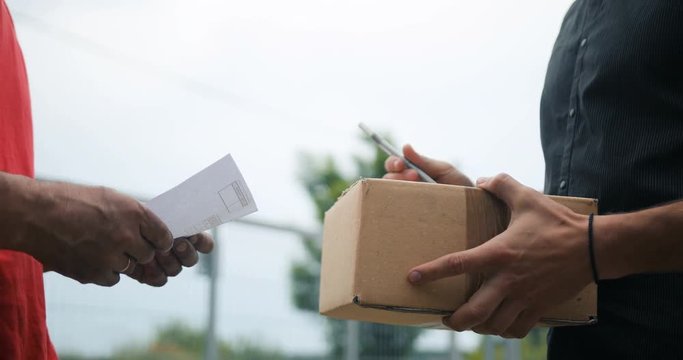 Signing for getting package. Young delivery man delivering a cardboard box courier
