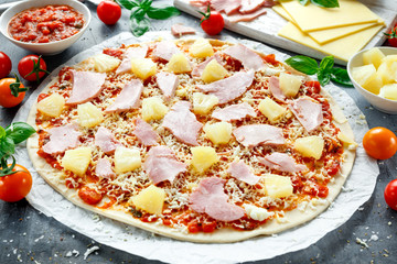 Ready to cook hawaii pizza with ham and pineapple, basil, tomatoes on backed paper