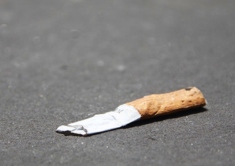 One cigarette laying on a floor. Gray asphalt on a background