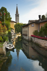 The tower bell of the cathedral of St. Nicolò is reflected on Livenza river in Sacile. Italy