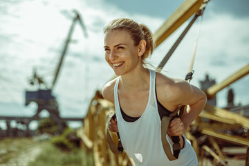 Portrait of young attractive woman does suspension training with fitness straps outdoors in urban city.