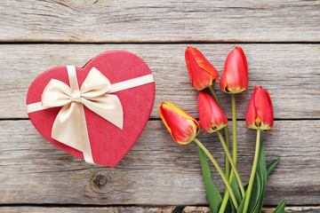Bouquet of red tulips with gift box on grey wooden table