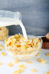 Pouring milk in bowl of cornflakes on wooden table