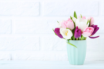 Bouquet of tulips in cup on brick wall background