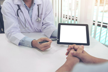 Doctor consulting patient and recommend treatment methods and how to rehabilitate the body, presenting results on tablet computer in hospital office