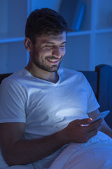 The happy man sit with a phone in the bed. night time