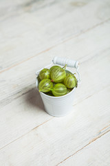 Juicy ripe berries of a gooseberry in a small basket on a wooden black surface. Gooseberry harvest. Gooseberry isolated on white background