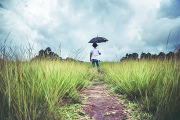 man standing umbrella On the green meadow in the rainy season. Asian man