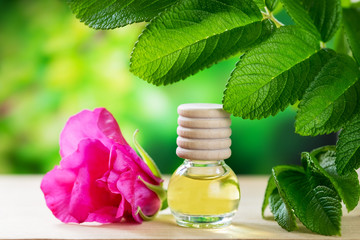 Essential rosehip oil in a glass bottle on the table amid foliage