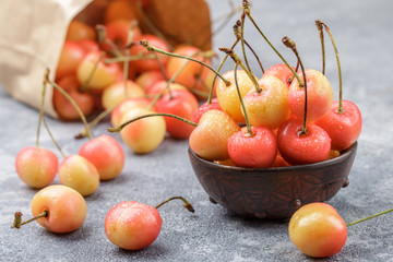 Red and yellow Rainier cherries with drops of water in a clay bowl on the gray concrete surface. Selective focus