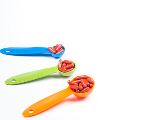 red capsules pills on colorful measuring spoon on white background. Increase the dosage of the medicine.