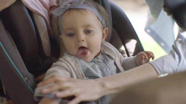 Mother Places Her Baby Girl In Car Seat, Puts Her Little Arm Through Strap, Begins To Buckle Her In