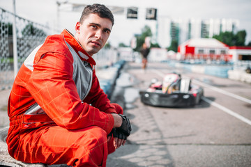 Karting racer sits on a tire, kart on background - obrazy, fototapety, plakaty