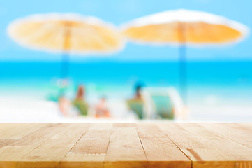 Fototapeta na wymiar Wood table top on blur beach background with parasols, summer holiday concept