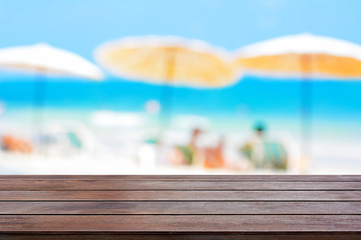 Wood table top on blur beach background with parasols, summer holiday concept
