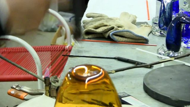 Glass artist separates punty from bottom of vase then heats bottom to soften with blowtorch to imprint company logo 