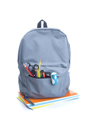 Backpack with school supplies on top of notebooks, isolated on white