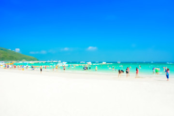 Blurred image of white sand beach with people in colorful cloth
