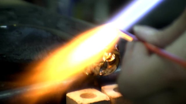 Close-up of tongue being added to glass snake as gaffer melts glass rod with blowtorch