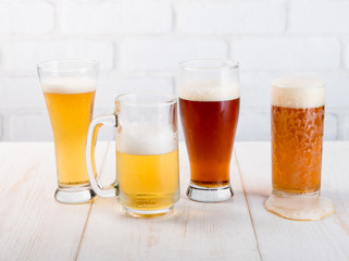 Beer glasses with various beer on wood table against white brick wall