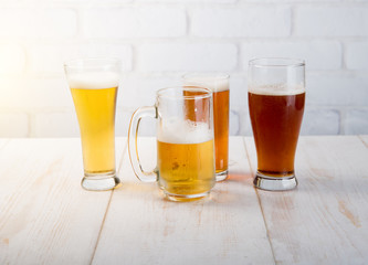 Beer glasses with various beer on wood table against white brick wall