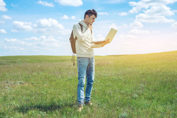 Naklejka na ściany i meble Young man sitting on a green meadow with laptop wireless on the background of blue cloudy sky