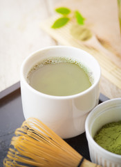 Green matcha tea in a bowl and bamboo whiskon on wood table