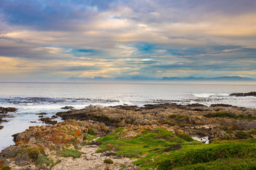 Rocky coast line on the ocean at De Kelders, South Africa, famous for whale watching. Winter season, cloudy and dramatic sky.