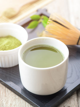 Green matcha tea in a bowl and bamboo whiskon on wood table