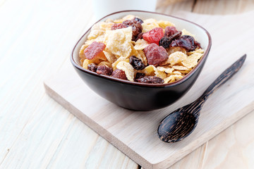 cornflakes and dry berry fruits in a brown bowl on a wooden background.
