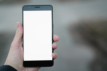 man hand holding smartphone with white screen outdoors with asphalt blurred background