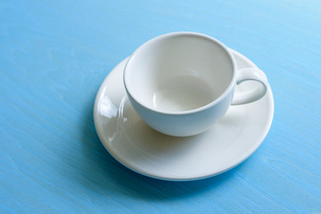 Empty white coffee cup with saucer on blue wood table