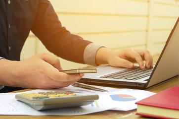 young accountant or business man using smartphone with calculator, data sheet, laptop on desk, analyzing and calculate, savings, finances, economy concept, sunlight effect, soft focus, selective focus