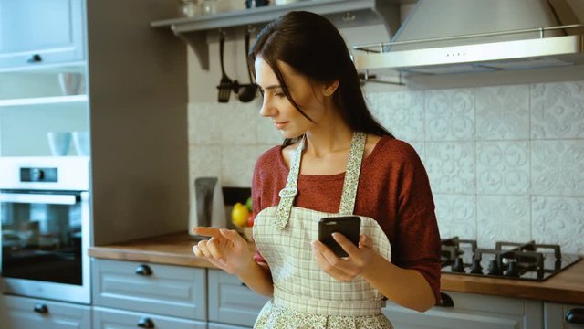 Young attractive woman using smartphone, reading recipe and checking ingredients for cooking. Close up