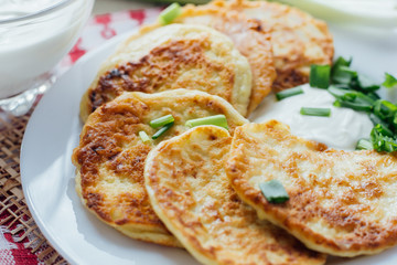 Vegetable fritters with sour cream and chopped leek on white plate 
