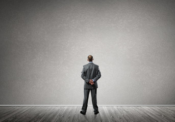 Obraz premium Businessman with hands behind his back and looking at blank concrete wall