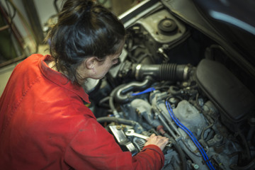 Fototapeta na wymiar Female mechanic inspecting car engine with wrench