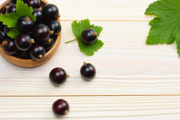 black currant in wooden bowl with green leaf on white wooden background. top view with copy space